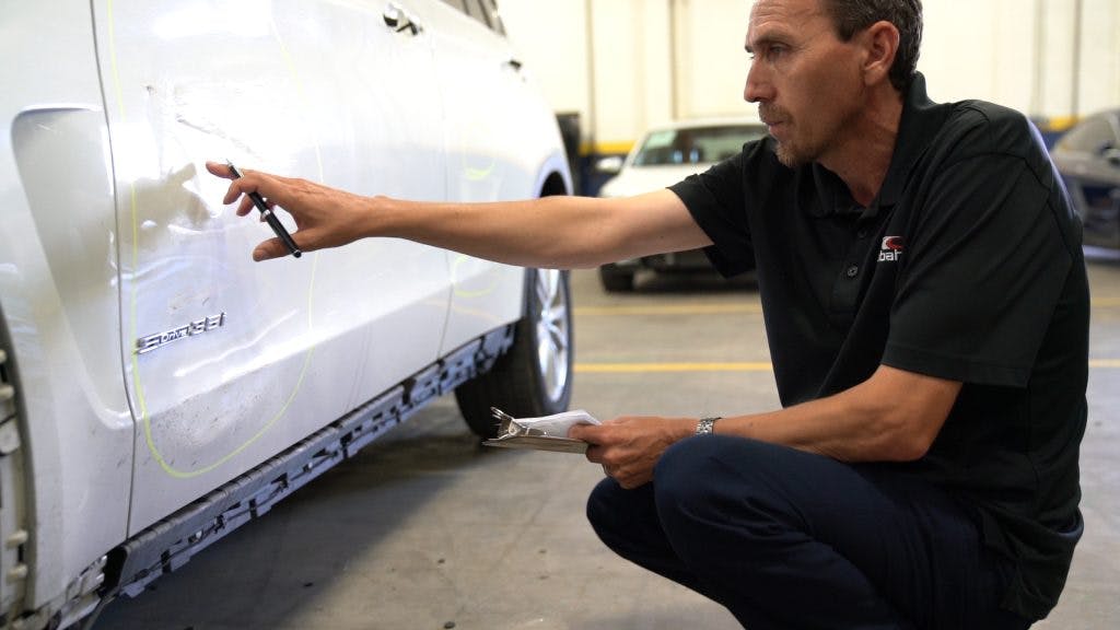 A man is inspecting customers car for scratches at the ICC Collision Center.